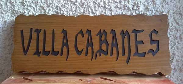 Cartel de madera rectangular con bordes irregulares que lleva texto grabado y pintado